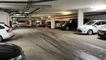 Geräumige Tiefgarage mit zahlreichen Stellplätzen und sichtbaren Installationen an der Decke.