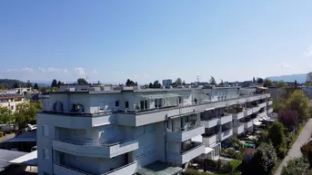 Luftaufnahme eines modernen Mehrfamilienhauses mit mehreren Balkonen, Dachterrassen und Carports.