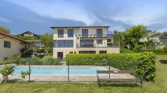Modernes Haus mit großem Pool und gepflegter Hecke im Gartenbereich unter blauem Himmel.