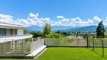 Moderne Architektur mit gepflegtem Rasen und beeindruckendem Bergblick unter blauem Himmel.