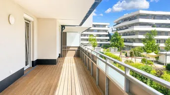 Heller Balkon mit Holzboden und Blick auf die moderne Wohnanlage.