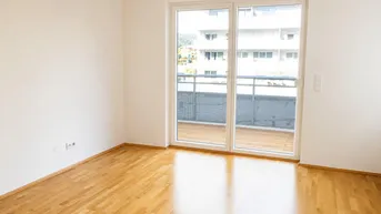Helles Zimmer mit Parkettboden und großem Fenster, das Zugang zu einem Balkon bietet.