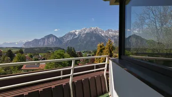 Sonniger Balkon mit atemberaubendem Bergblick und weitreichender grüner Landschaft unter blauem Himmel.