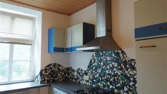 Küche mit Holzbalkendecke, farbenfroher Mosaik-Rückwand und integriertem Kochfeld.