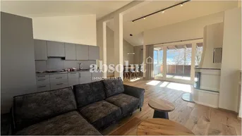 Geräumiger Wohnbereich mit offener Küche, Kamin und Zugang zu einem großen Balkon.