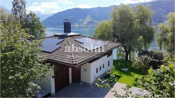 Haus am Seeufer mit Solarpaneelen auf dem Dach und Bergblick in idyllischer Lage.