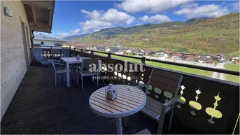 Großer Holzbalkon mit Esstisch und Liegestühlen, bietet weite Aussicht auf die Landschaft.
