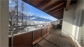 Langer Holzbalkon mit Geländer und beeindruckendem Blick auf die verschneite Bergwelt.