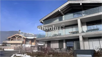 Modernes Gebäude im alpinen Stil mit Holzelementen, Glasbalkonen und verschneiter Umgebung.