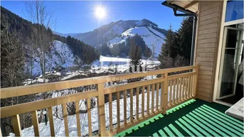 Sonniger Balkon mit Holzbalkongeländer und weitem Blick auf die verschneiten Berge.