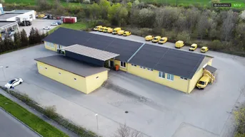Luftaufnahme eines gelben Gewerbegebäudes mit großem Parkplatz und vielen Lieferwagen.