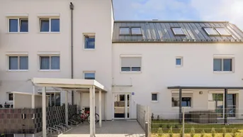 Modernes Mehrfamilienhaus mit weißer Fassade, Carport und Fahrradstellplätzen unter blauem Himmel.