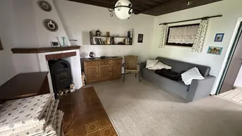 Gemütliches Wohnzimmer mit Kamin, Teppichboden und rustikaler Holzbalkendecke.