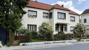 Einfamilienhaus mit rotem Ziegeldach, heller Fassade und Vorgarten an einer ruhigen Straße.