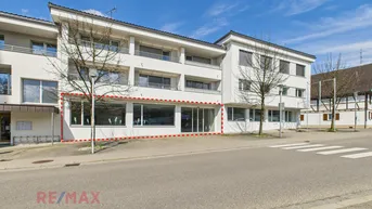 Außenansicht eines modernen Geschäftsgebäudes mit großen Schaufenstern und einer roten Umrandung.