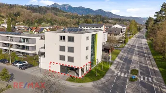 Luftaufnahme eines modernen Geschäftsgebäudes mit umliegender Infrastruktur und Bergpanorama im Hintergrund.