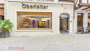 Fassade eines Geschäftsgebäudes mit großem Schaufenster, gepflastertem Vorplatz und traditioneller Architektur.