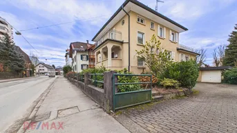 Traditionelles Wohnhaus mit gelber Fassade, weißen Fensterläden und Vorgarten an einer Straße gelegen.