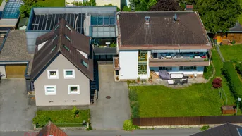 Luftaufnahme von zwei Wohnhäusern mit Gärten und umliegender Bebauung unter blauem Himmel.