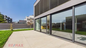 Geräumige Terrasse mit hellem Fliesenboden und Zugang zum Garten, umgeben von moderner Architektur.