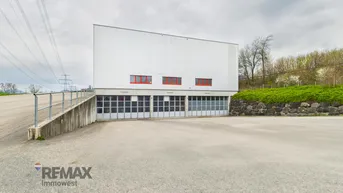 Modernes Industriegebäude mit mehreren Garagentoren und einer Zufahrtsrampe unter bewölktem Himmel.