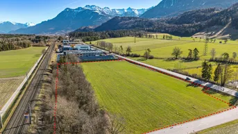Luftaufnahme eines großen Grundstücks mit grünen Feldern, umgeben von Bergen und einer Straße.