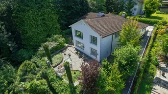 Luftaufnahme eines weißen Hauses mit Ziegeldach, umgeben von üppigem Grün und einem gepflasterten Gartenbereich.