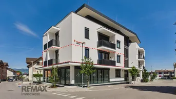 Modernes Gebäude mit weißer Fassade, großen Fenstern und mehreren Balkonen, umgeben von Grünflächen.