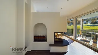 Gemütlicher Wohnbereich mit Kachelofen, Holzboden und großen Fenstern zur Terrasse.