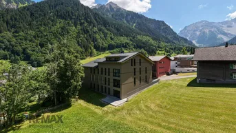 Modernes Mehrfamilienhaus in alpiner Umgebung mit grünen Wiesen und Bergblick.