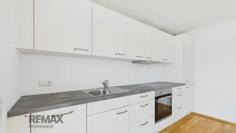 Moderne Einbauküche mit weißen Schränken, grauer Arbeitsplatte und integrierten Geräten.