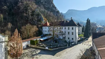 Luftaufnahme eines historischen Gebäudes mit umliegender Landschaft und Bergen im Hintergrund.