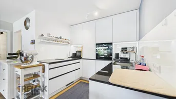 Moderne, weiße Einbauküche mit Hochglanzfronten und dunkler Arbeitsplatte.