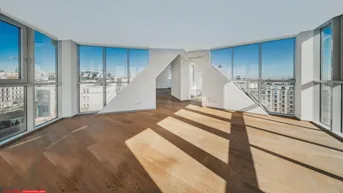 Helles, leeres Zimmer mit Holzboden und großen Fenstern, die viel Tageslicht hereinlassen.