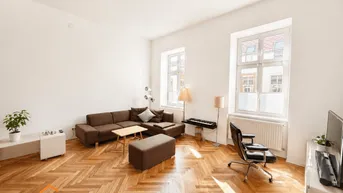 Helles Wohnzimmer mit Fischgrätparkett, hohen Decken und großen Fenstern, modern eingerichtet.