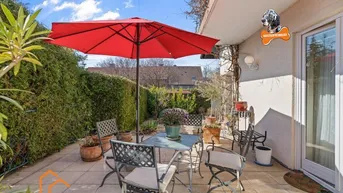 Gemütliche Terrasse mit Gartenmöbeln und rotem Sonnenschirm, umgeben von grünen Hecken.