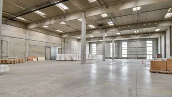 Große, leere Lagerhalle mit hohen Decken, Betonwänden und Oberlichtern, bereit zur Nutzung.