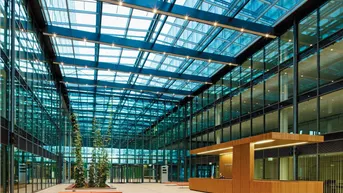 Großzügiges, modernes Atrium mit Glasdach, Rezeption und viel Tageslicht, ideal für Empfangsbereiche.