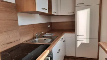 Moderne Einbauküche mit hellen Fronten, Holzoptik-Arbeitsplatten und integriertem Kochfeld.