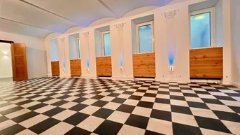 Geräumiger, loftartiger Raum mit auffälligem schwarz-weißem Schachbrettmuster-Boden, hohen Gewölbedecken und dekorativen Säulen.