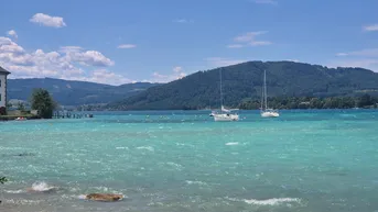 Atemberaubender Blick auf den türkisfarbenen See mit Segelbooten und bewaldeten Bergen im Hintergrund.