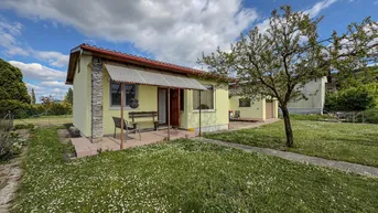 Kleines Einfamilienhaus mit gelber Fassade und Vorgarten unter blauem Himmel.