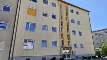 Mehrstöckiges Wohngebäude mit gelber Fassade und mehreren Fenstern unter blauem Himmel.