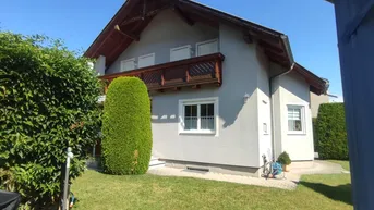 Seitenansicht des Hauses mit gepflegtem Rasen und hohen Hecken unter blauem Himmel.