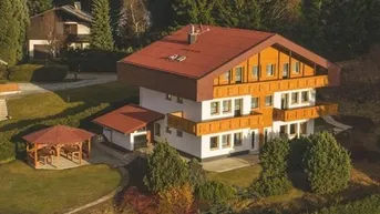 Haus im alpinen Stil mit Holzbalkonen und einem Gartenpavillon in grüner Umgebung.