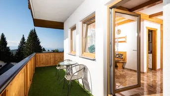 Balkon mit Kunstrasen, Sitzgelegenheiten und Zugang zum Innenbereich, umgeben von Natur.
