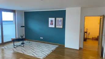 Helles Wohnzimmer mit Holzboden, einer blauen Akzentwand und großem Fenster.