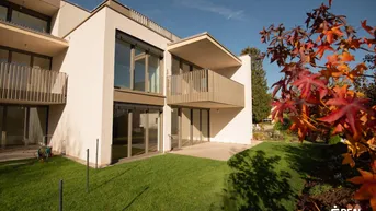Moderne Fassade mit Balkon und großzügiger Rasenfläche, umgeben von Herbstlaub.
