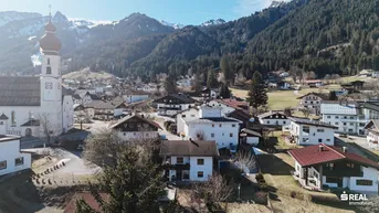 Panoramablick auf ein malerisches Dorf in den Alpen mit traditionellen Häusern und einer Kirche.