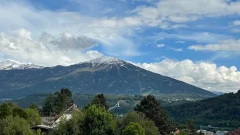 Panoramablick auf schneebedeckte Berge und grüne Landschaft unter blauem Himmel.